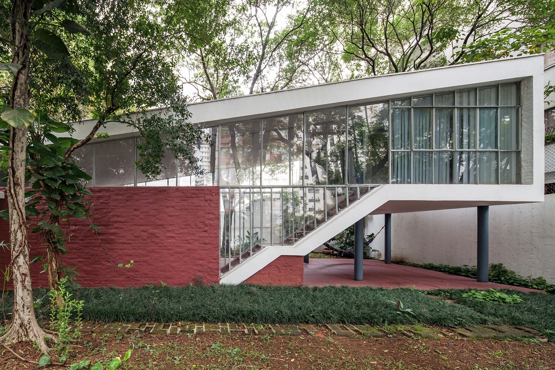 Na fachada frontal é possível ver o estúdio do arquiteto (à dir.), apoiado sobre os pilotis. O ambiente é alcançado pela escada em dois lances com fechamento em vidro. Destaque, ainda para a inclinação da laje de cobertura, chamada "borboleta". A Casa do Arquiteto (1949) foi projetada por João Batista Vilanova Artigas, que completaria 100 anos em 23 de junho de 2015 - Leonardo Finotti/ UOL