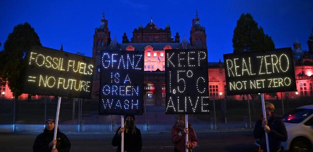 Ativistas pelo clima seguram cartazes iluminados contra o uso de combustíveis fósseis na COP26 em Glasgow, na Escócia