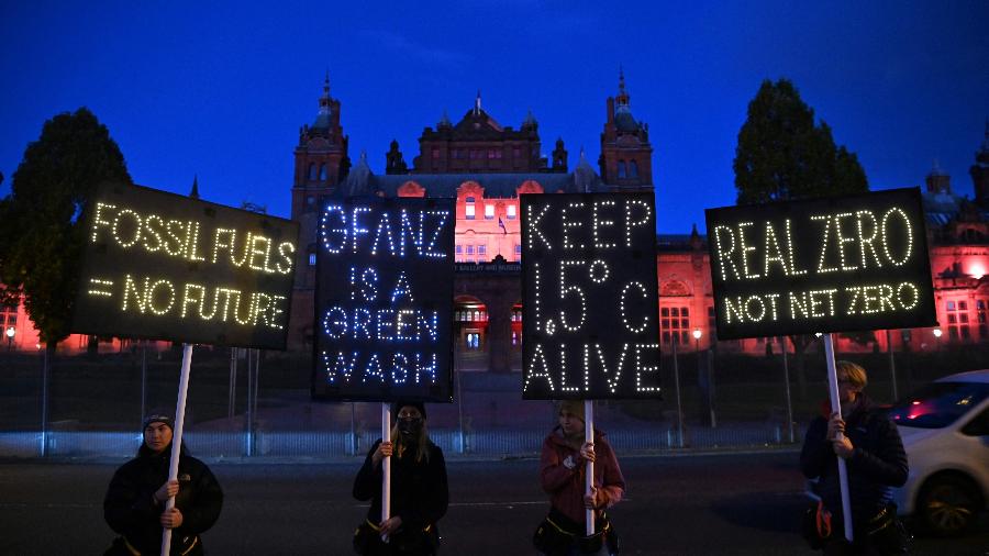 Ativistas pelo clima seguram cartazes iluminados em manifestação contra o uso de combustíveis fósseis durante a COP26 em Glasgow, na Escócia - Ben Stansall/AFP
