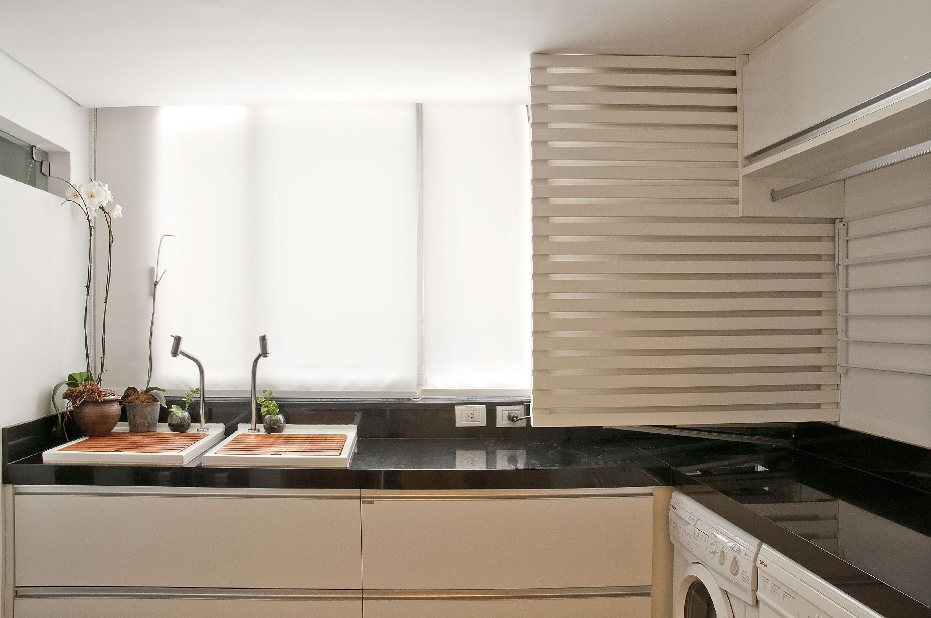 A bancada de granito preto em L otimizou o espaço da área de serviço e as arquitetas da Triarq Studio ainda conseguiram alocar dois pequenos tanques. Enquanto um deles permite deixar algumas roupas de molho, o outro possibilita esfregar, quando necessário, as demais peças. Há diversas gavetas para ajudar na organização - Carlos Mancini | Divulgação