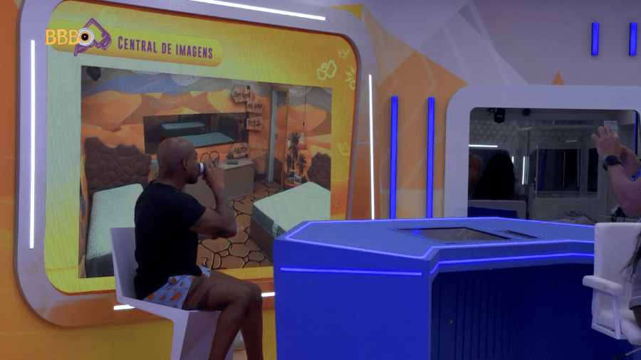 BBB 23: Cezar posa com cerveja em frente a imagem do Quarto Deserto desocupado - Reprodução/Globoplay