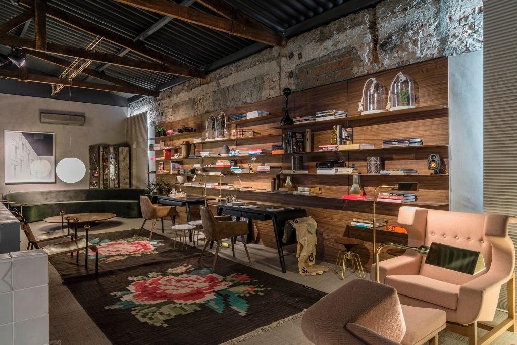 A Biblioteca, da arquiteta Cláudia Zuppani, mede 80 m² e conta com vários elementos rústicos, como as tesouras aparentes do telhado e as paredes parcialmente sem acabamento. As cadeiras são vistas em blocos na decoração: duas poltronas em couro (à esq.), duas junto às mesas pretas e duas rosa, com recortes setentistas. A paleta de marrons e amadeirados rege a ambientação - Jomar Bragança/Divulgação