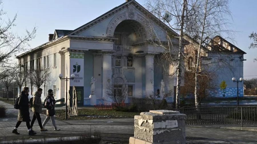 Pessoas passam pela Casa da Cultura danificada em Irpin, a noroeste de Kiev, em 23 de dezembro de 2022, em meio à invasão russa da Ucrânia