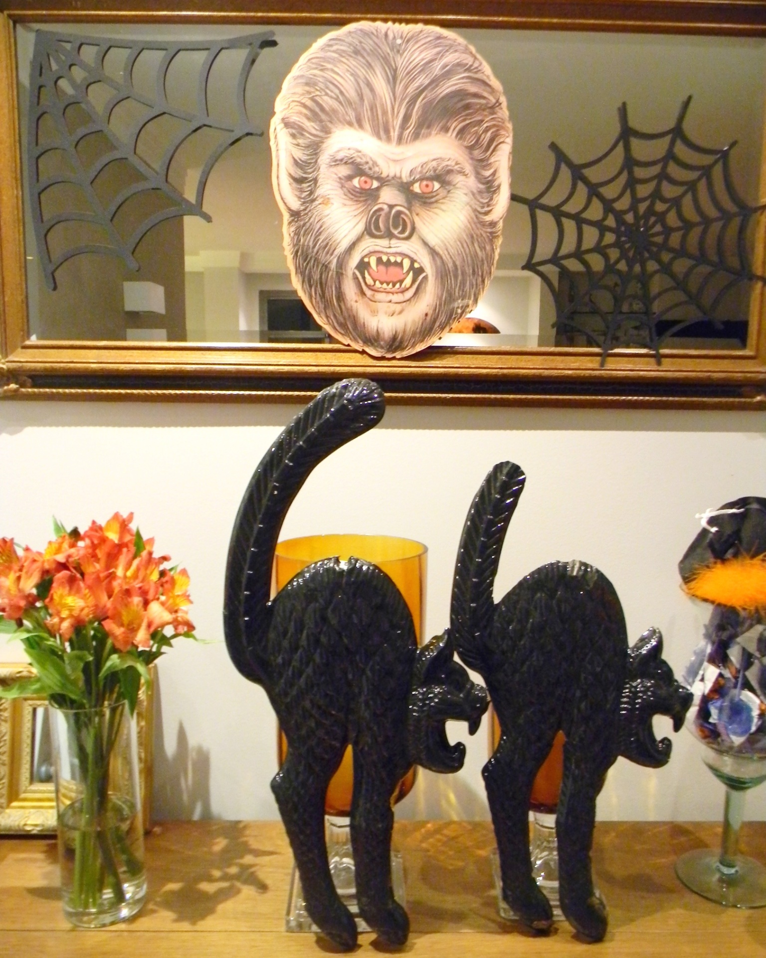 A decoração do hall da entrada desta festa de adolescente com tema Halloween tinha um espelho com máscara de lobisomem e teias de aranha feitas de scrapbook, além de dois gatos pretos e um buquê de astromélias na cor laranja. Pirulitos que manchavam a língua foram colocados em um vaso - Divulgação