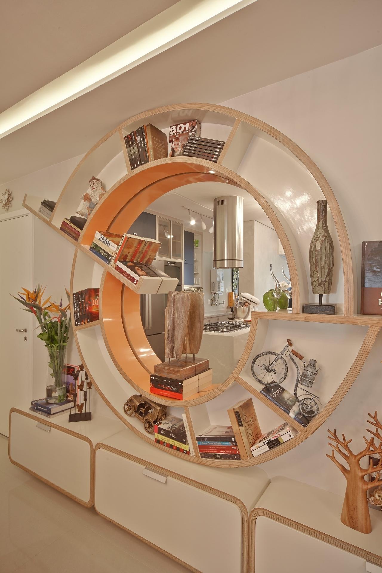 Que tal uma minibiblioteca na cozinha? Foi a ideia do designer de interiores Henrique Freneda para deixar os livros de receita do morador à mão. Ele apostou no inusitado formato, obtido graças às chapas de compensado (8 lâminas) mantidas na prensa por dias na prensa. A estrutura foi laqueada em off-white. Contornando o espelho do centro, o laranja reforça a luminosidade na peça. - Divulgação