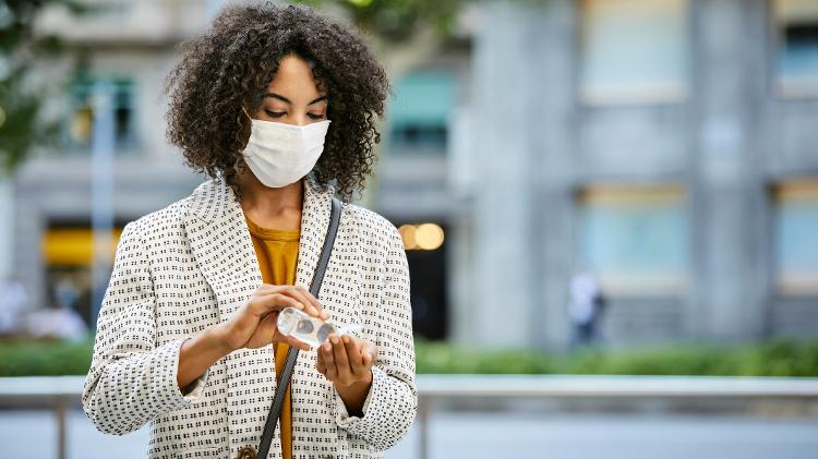 máscara, álcool em gel, cuidados, covid, pandemia, mulher de máscara usando alcool em gel - Getty Images - Getty Images