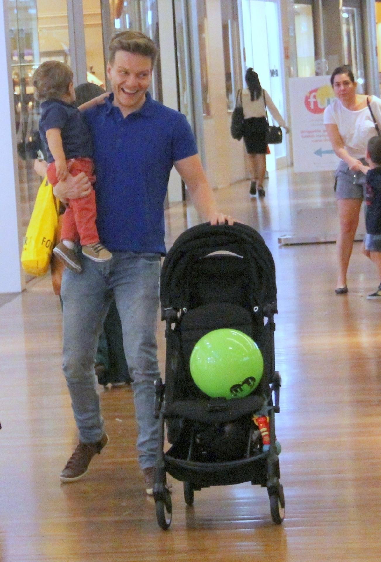 Depois de um tempo, Teodoro cansou de andar livre pelos corredores do shopping e preferiu seguir o passeio no colo do papai coruja Teló  - AgNews/J Humberto