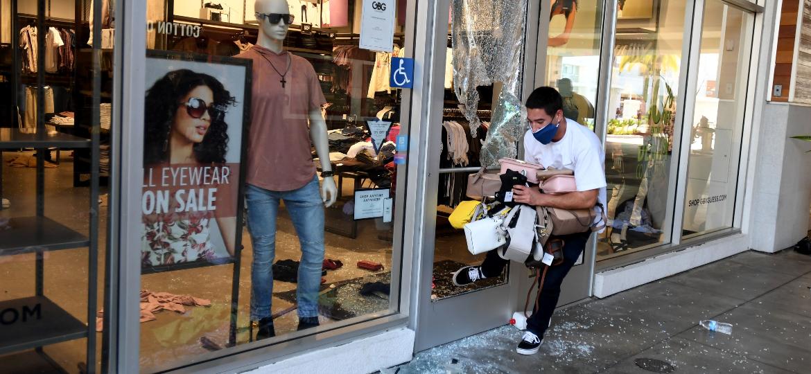 Homem carrega diversas bolsas de uma loja da Guess após protestos em Los Angeles - Getty Images