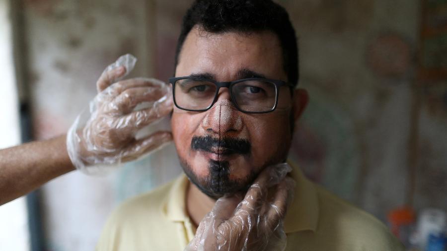 Jorge Roriz pinta a parte inferior do rosto da pessoa em uma máscara branca - REUTERS/Pilar Olivares