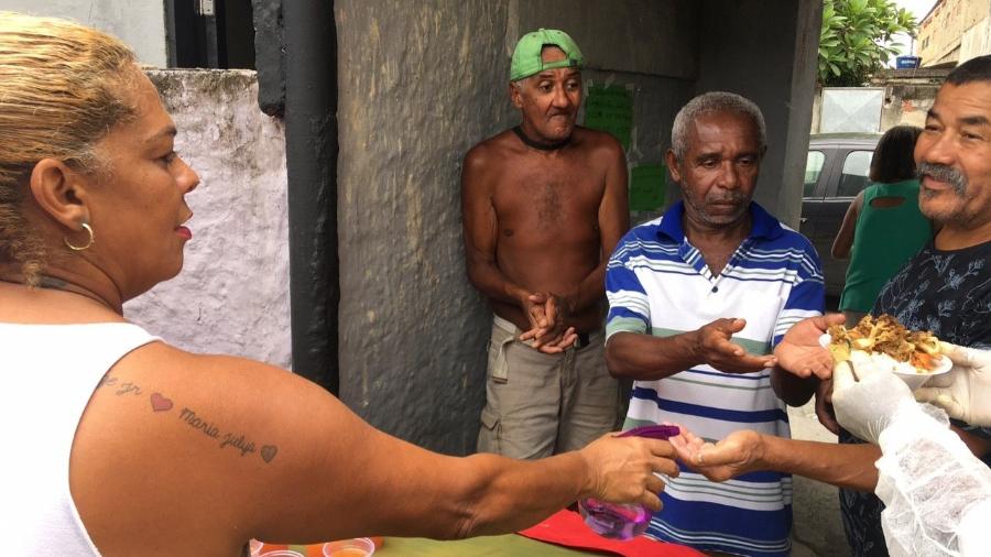 Celi borrifa álcool nas mãos dos moradores antes da refeição - Fabiana Batista/UOL