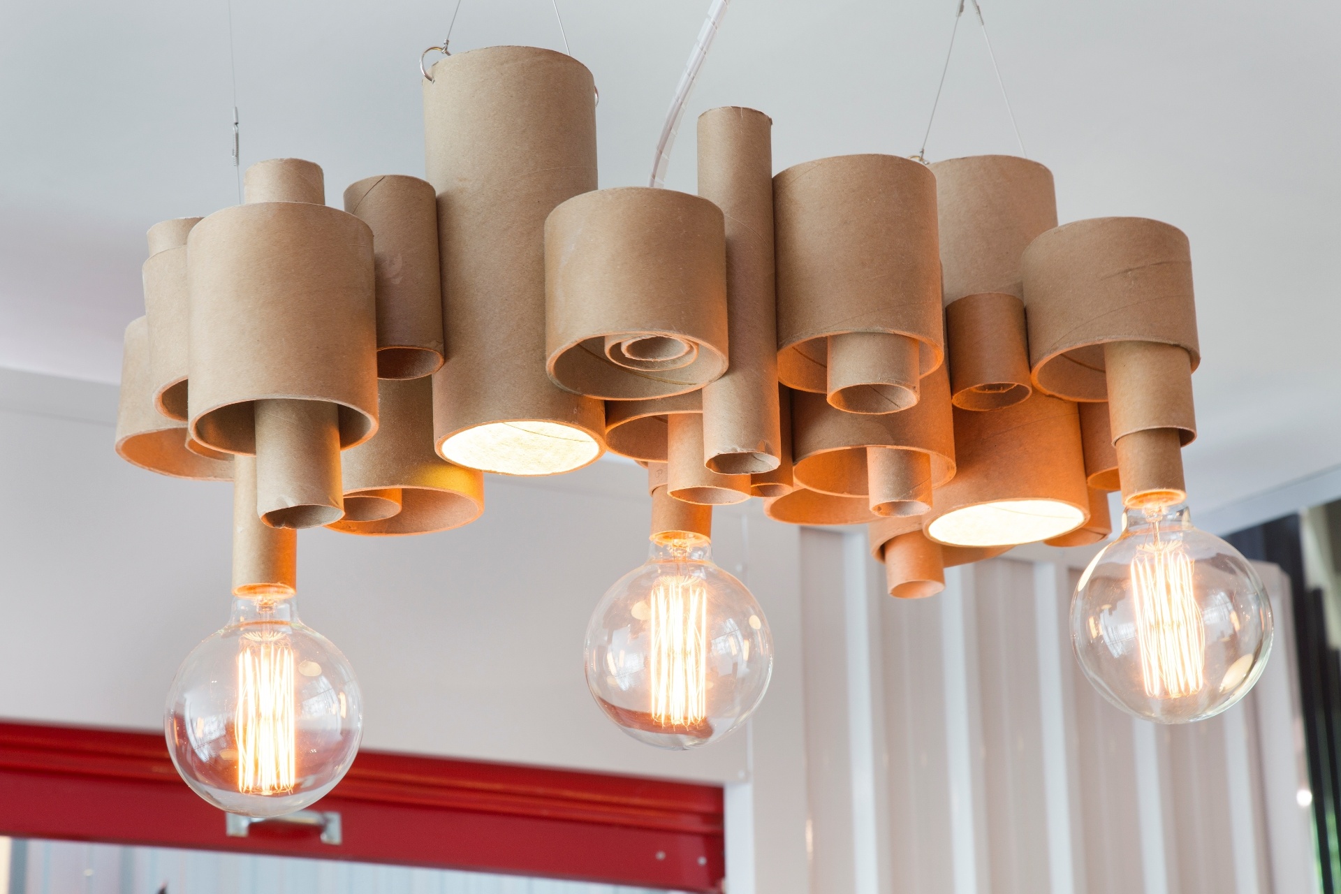 Materiais descartáveis podem virar luminárias incríveis, basta um pouco de criatividade e uma boa dose de capricho. A arquiteta Isabela Saramago, por exemplo, montou para o Espaço Alternativo Metromax, da Morar Mais por Menos RJ, o lustre Ameba com tubos de papelão usados pela indústria têxtil. As lâmpadas com filamentos de carbono reforçam a pegada industrial da peça | A mostra (www.morarmais.com.br) fica em cartaz até 2 de novembro de 2015 - MCA Estúdio/ Divulgação