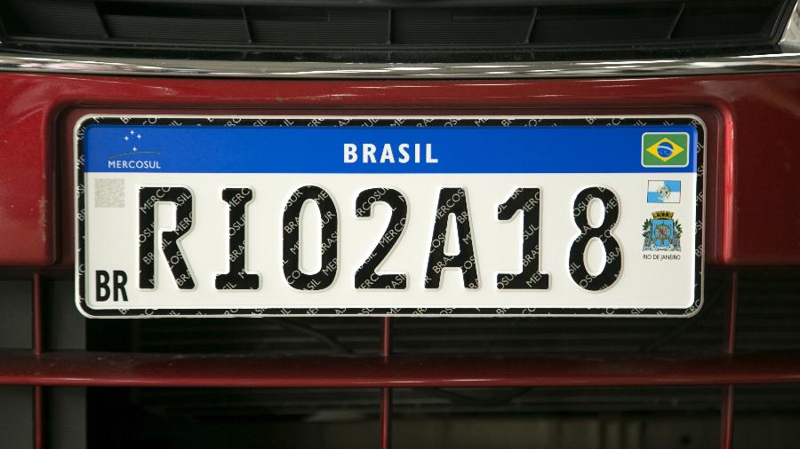 Placa Mercosul original, lançada no Rio de Janeiro em 2018, trazia a bandeira do estado e o brasão do município de registro do veículo, mas item foi removido no mesmo ano sob alegação de redução de custos Placa Mercosul original, lançada no Rio de Janeiro em 2018, trazia a bandeira do estado e o brasão do município de registro do veículo, mas item foi removido no mesmo ano sob alegação de redução de custos