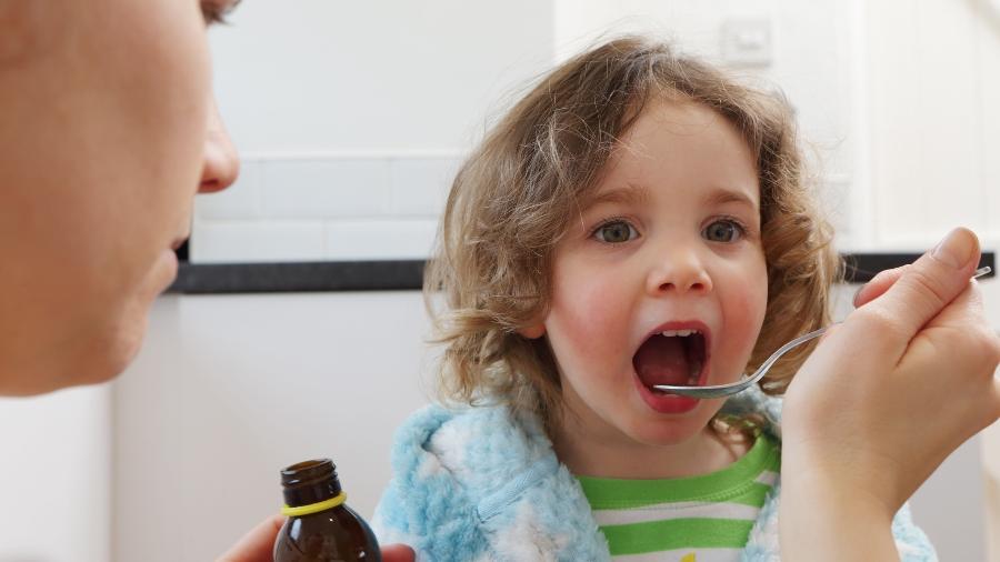 Adulto medicando criança com colher para medir remédio - Peter Cade/ Getty Images