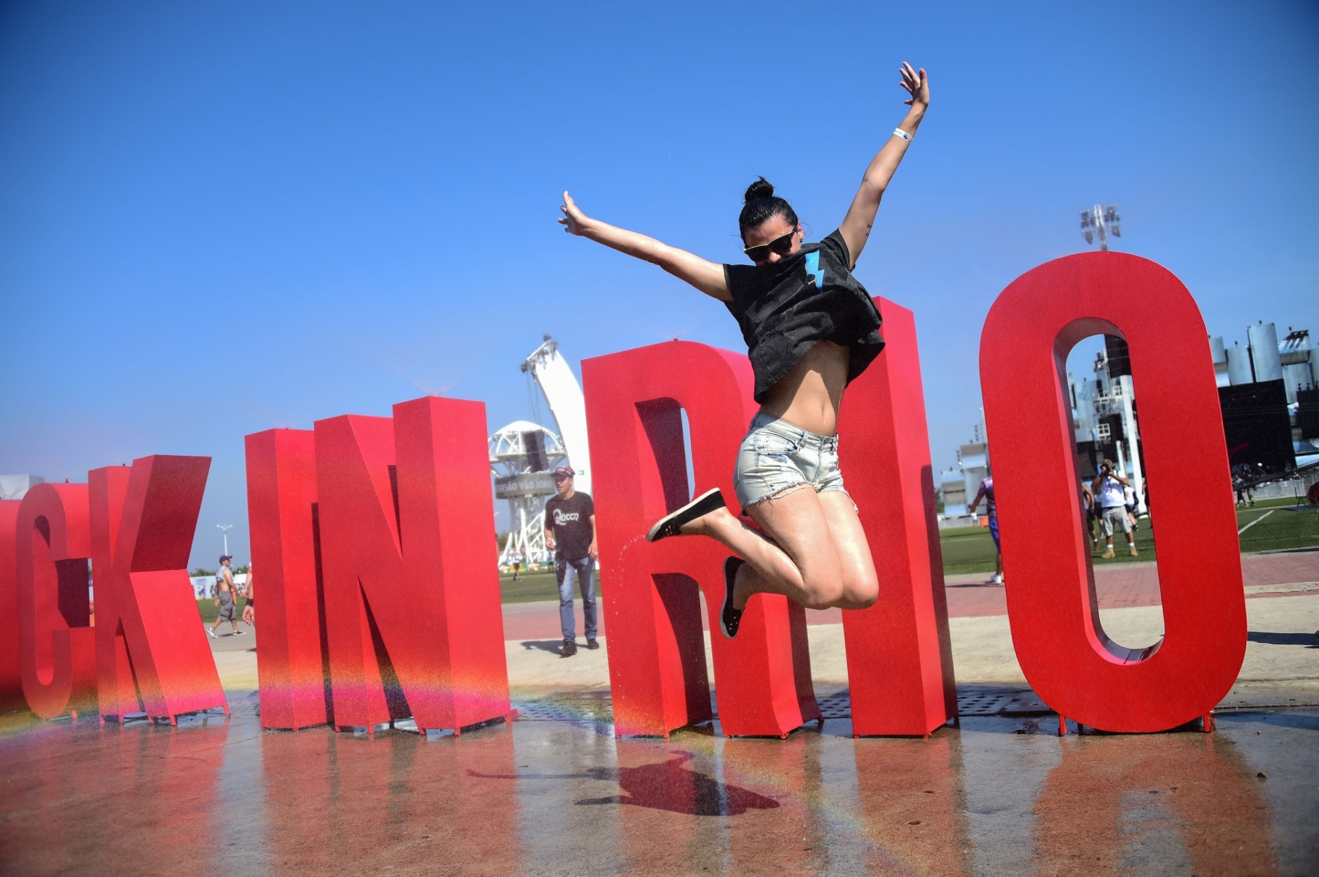 18.set.2015 - Com a temperatura batendo os 38º C e sensação térmica de 40º C, público que chega à Cidade do Rock, para curtir o primeiro dia de Rock in Rio, tenta se refrescar do jeito que pode, até com banho em fonte que espirra água - Christophe Simon/AFP