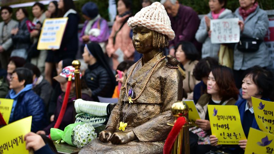 Protestantes se sentam ao lado da estátua de uma jovem sul-coreana, símbolo da lembrança das mulheres forçadas a servirem como escravas sexuais para solados japoneses durante a 2ª Guerra Mundial - AFP