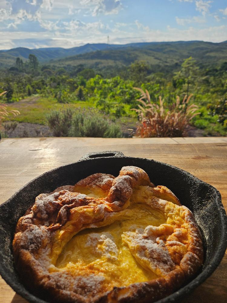 Depois de sair 'inflada' do forno, a panquecona murcha: é a hora de colocar os complementos, como mel e frutas Depois de sair 'inflada' do forno, a panquecona murcha: é a hora de colocar os complementos, como mel e frutas