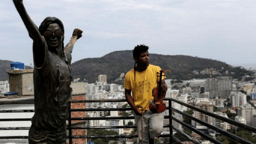 Paulo Maurício Dias posa para foto segurando seu violino ao lado da estátua de Michael Jackson na favela Santa Marta, no Rio - Bruno Kelly/Reuters