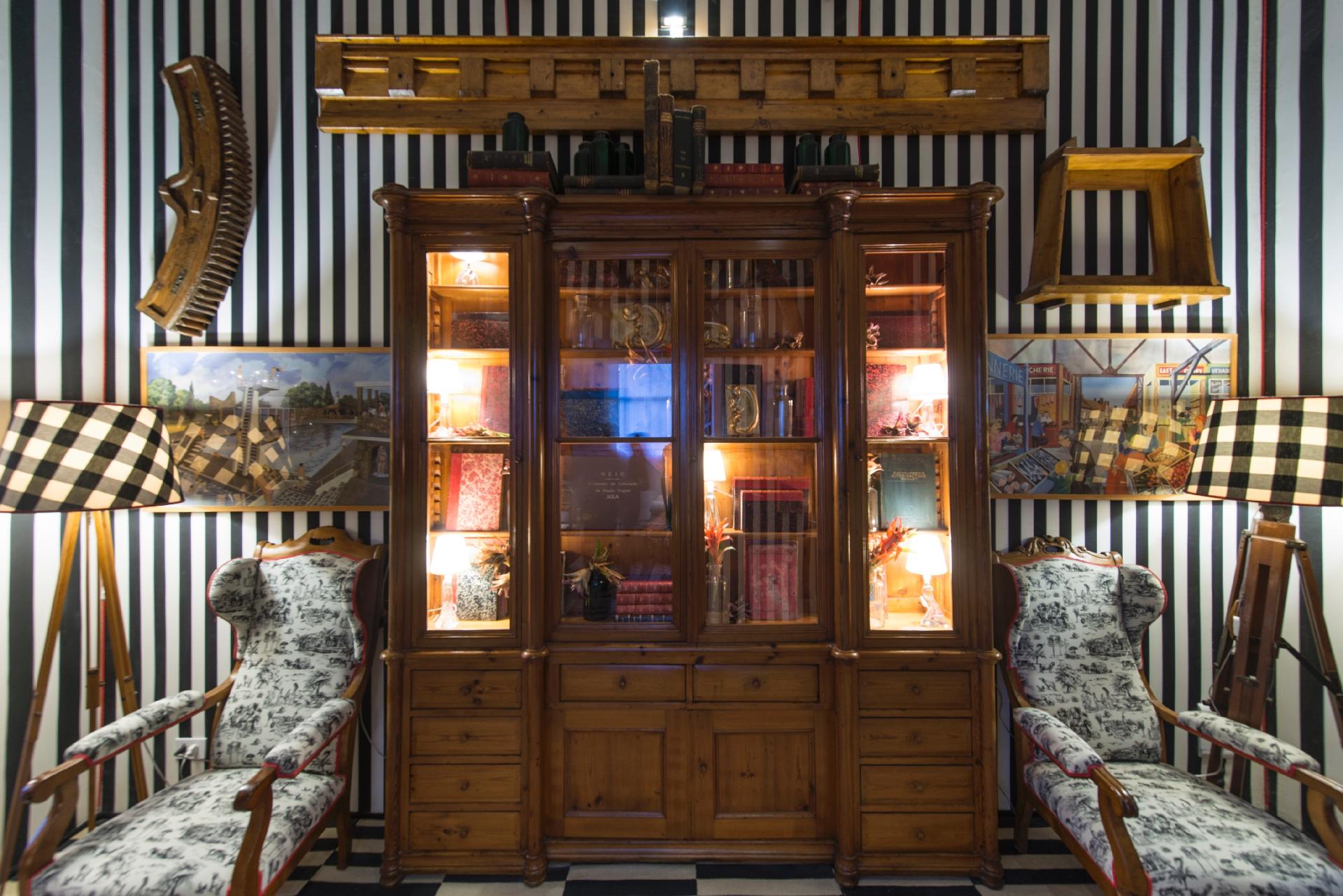 Os móveis da Circulação, assinada pela arquiteta Luciana Kreimer na edição paulistana da Casa Cor SP 2016, são do antiquário Arnaldo Danemberg (www.arnaldodanemberg.com.br) e fazem referência à história paulistana. Destaque para a estante disposta no centro do espaço, feita com madeira portuguesa. Nas duas laterais, poltronas com estampa 'toile de jouy' e luminárias com cúpulas xadrezes - Katia Kuwabara/UOL