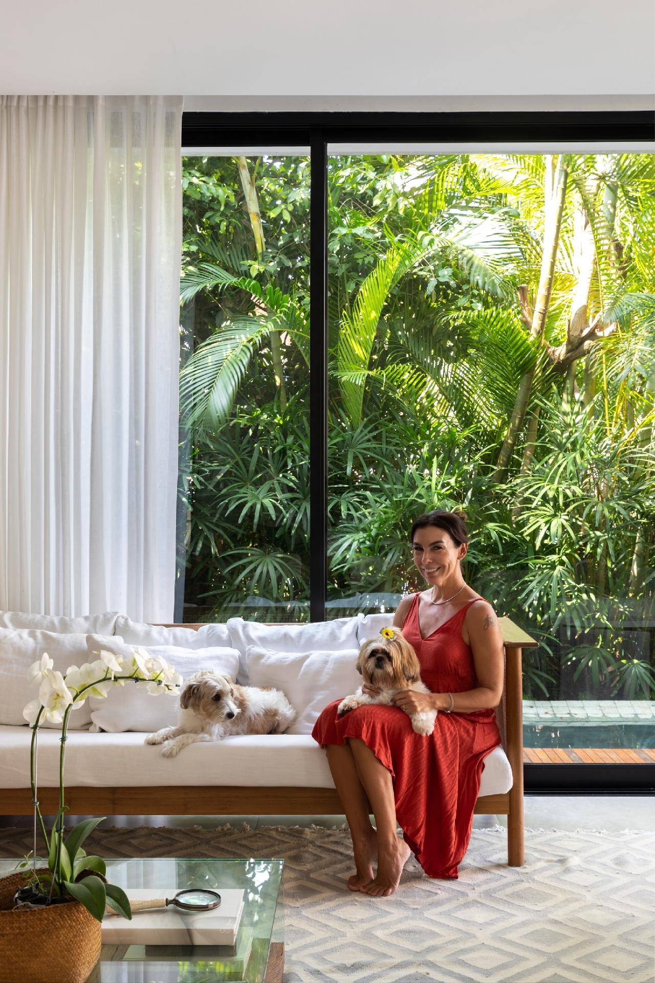 Com os cães Matilda e Kobe, a moradora Aline Veiga posa na sala, no sofá branco - veja que o verde do jardim colore a casa. - Luiza Schreier/Divulgação