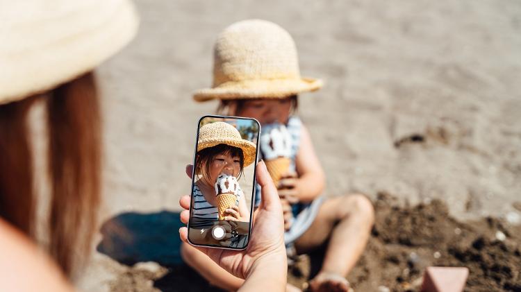 Mãe tira foto de filha tomando sorvete/ Mãe fotografa filha na praia/ Mãe tirando foto de criança