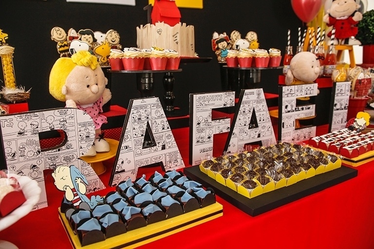 As placas em MDF com o nome do aniversariante foram forradas com quadrinhos do Snoopy e sua turma. As peças foram confeccionadas especialmente para a festa pela Caraminholando. A decoração da mesa também contou com bonecos de pelúcia dos personagens do desenho - Divulgação