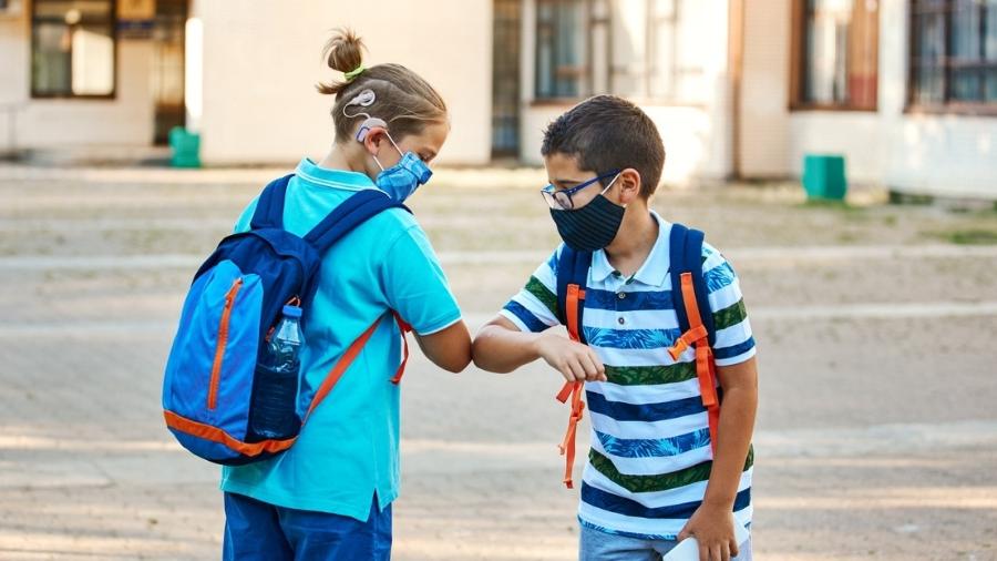 Crianças de máscara na escola se cumprimentam; foto ilustrativa - iStock