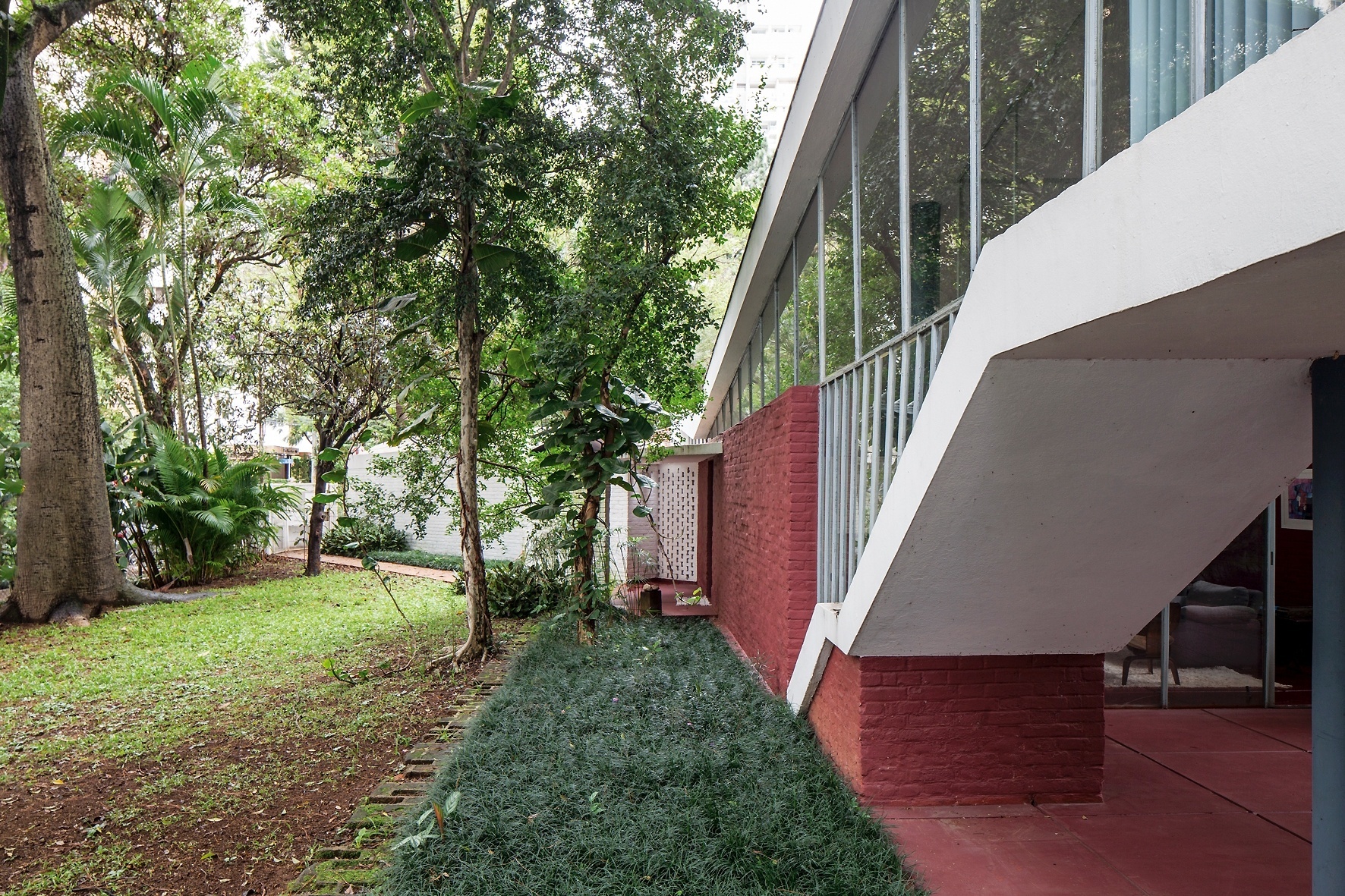 A Casa do Arquiteto (1949), projetada por João Batista Vilanova Artigas (1915-1985), conta com um bloco "anexo" com hall de entrada e parede vazada que delimita o acesso à lavanderia (ao fundo). O jardim com arbustos, gramado e árvores frondosas "é uma lembrança gostosa das brincadeiras dos meus tempos de criança", diz Rosa Artigas, historiadora e filha do arquiteto - Leonardo Finotti/ UOL