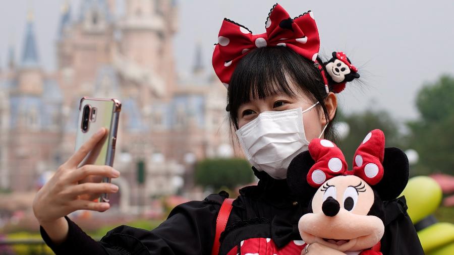 Visitante vestida de Minnie e usando máscara de proteção contra o coronavírus tira selfie na reabertura da Disney de Xangai - Aly Song/Reuters