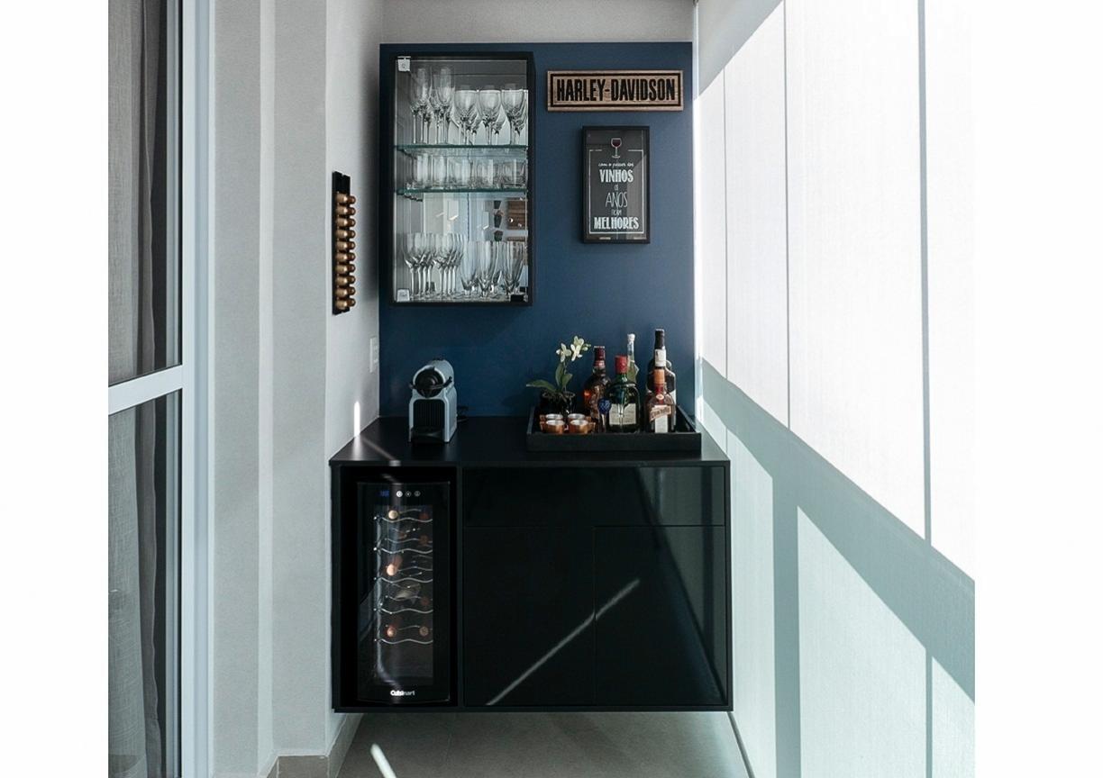 Os arquitetos Iris Filomena e Marcos Vaz aproveitaram o pequeno recuo da sacada e criaram um misto de cantinho do café e bar. O espaço abriga mini adega de vinhos, cristaleira para as taças e gavetas para utensílios. As paredes ainda receberam um quadro para colocar rolhas e um porta-cápsulas de café.  O fundo pintado de azul cria profundidade e ainda ressalta os móveis em MDF laqueado - Lucas Prado / Divulgação