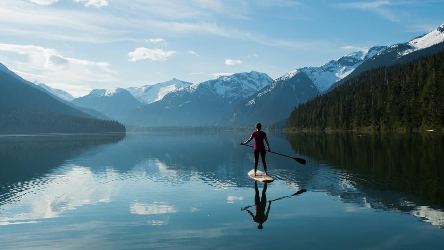 Mulher stand-up paddle embarcando em um lago de montanha intocada - Getty Images