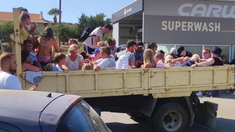 Turistas se amontoam em uma carreta durante a evacuação devido aos incêndios na ilha de Rodes, na Grécia, no sábado (22) - STRINGER/AFP