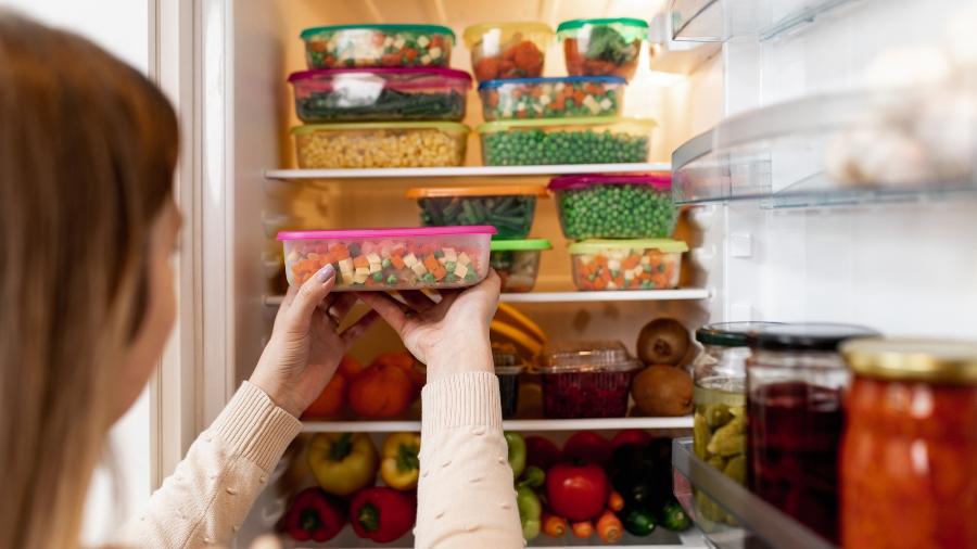 Mulher guardando alimentos em geladeira organizada - Getty Images