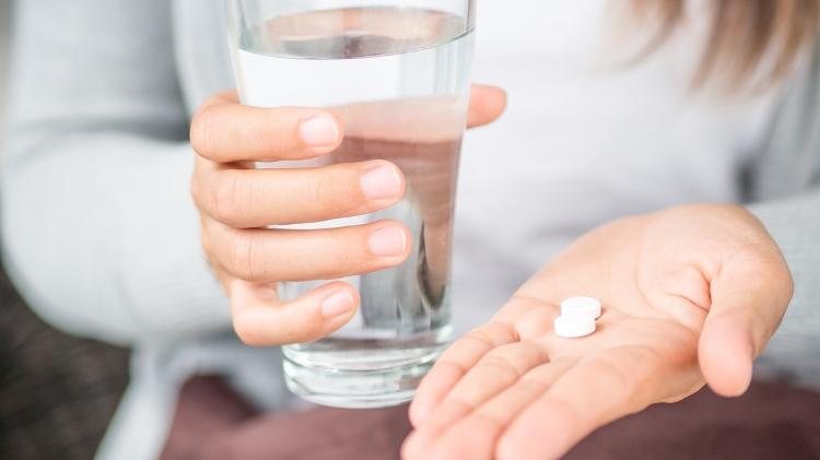 Mão segurando remédio, comprimido, medicamento, copo de água com remédio - iStock - iStock