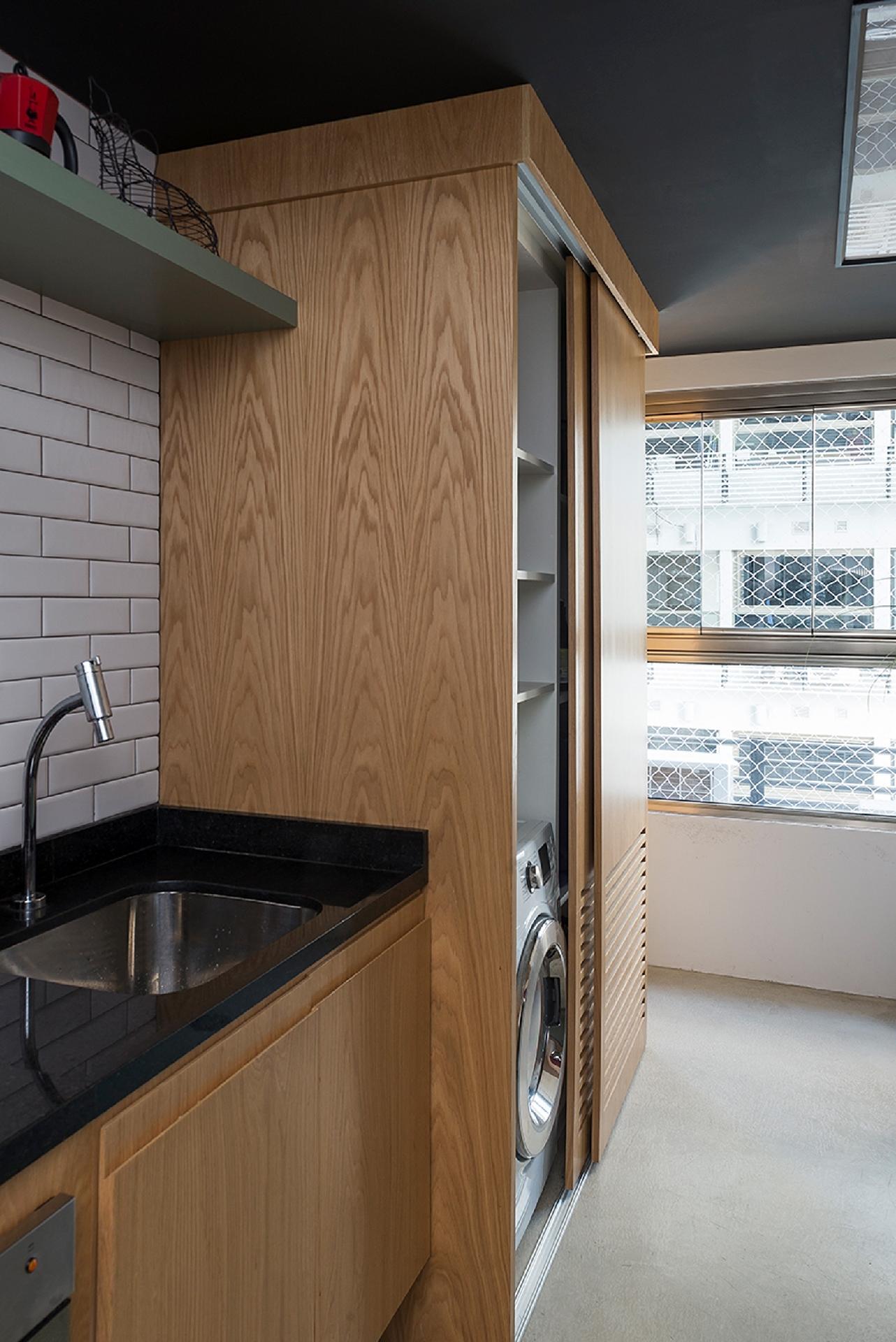 Em apartamentos pequenos, cozinhas e lavanderias costumam ficar bem juntinhas. Neste projeto da Ah!Sim não foi diferente, por isso os profissionais planejaram a marcenaria para isolar visualmente o local da máquina de lavar e seca. Portas de correr, que não ocupam espaço, dão acesso ao equipamento - Manu Oristânio | Divulgação