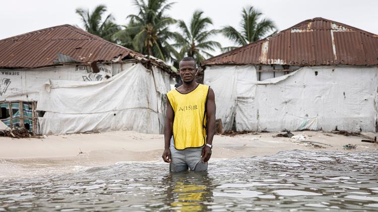 Hassan Kargbo em frente a duas casas durante a maré alta na Ilha Nyangai Hassan Kargbo em frente a duas casas durante a maré alta na Ilha Nyangai