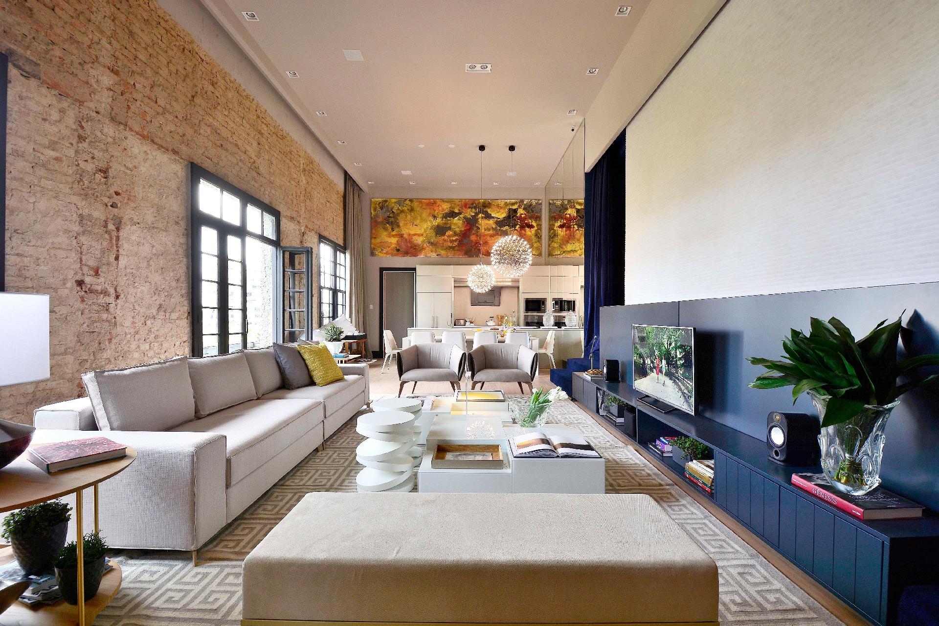 O Loft For Life, de Dany Bitencourt e Wagner Costa, deixou à mostra as paredes (à esq.) maciças originais do salão do Petrópole Tênis Clube, datadas de 1940. Com peças majoritariamente claras, o mobiliário é leve e presa por linhas retas, à exceção das mesas formadas por círculos (ao centro). Para acomodar o home theater, um móvel baixo, extenso e azul (à dir.) - Eduardo Liotti/ Divulgação