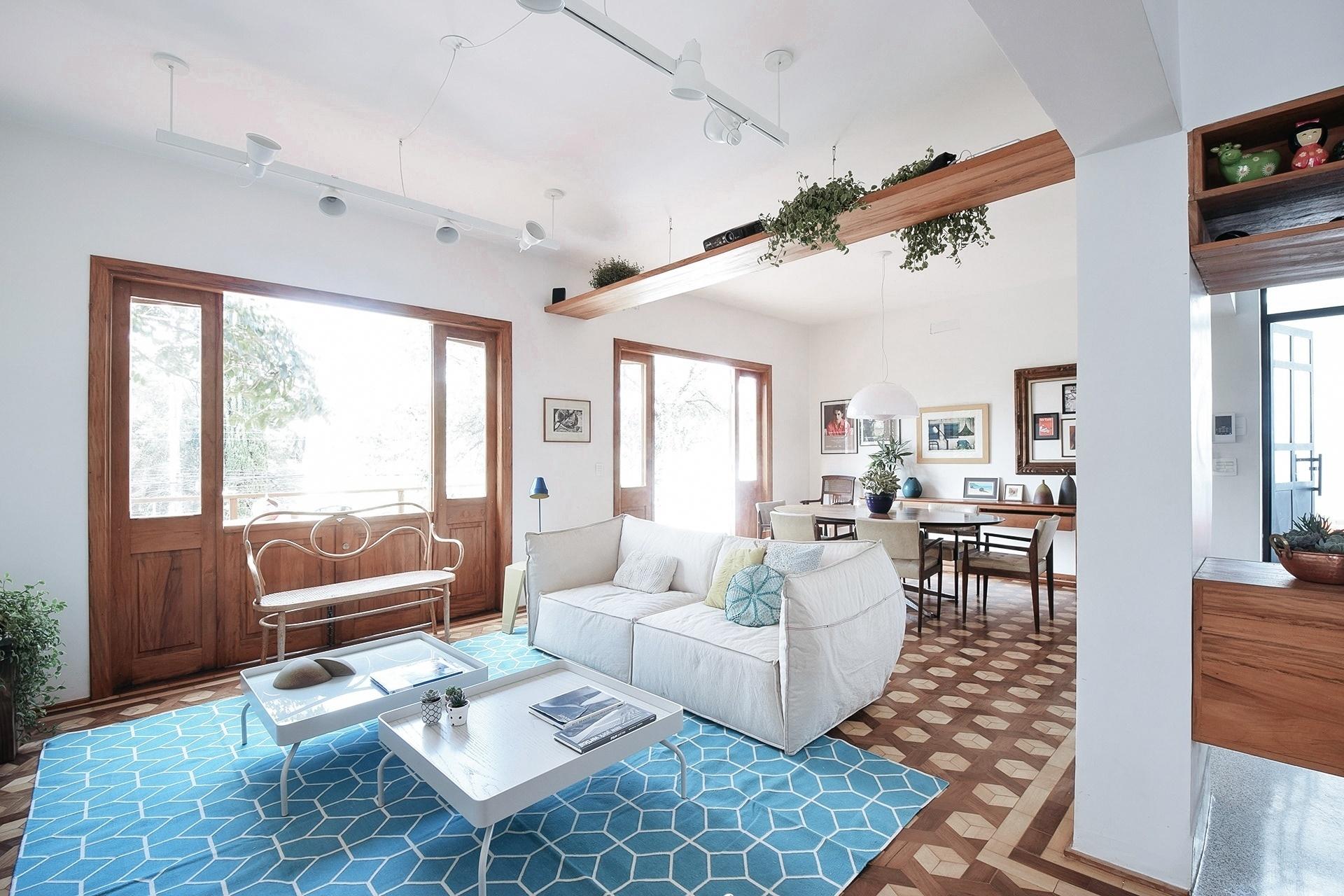 O a:m studio reaproveitou a madeira natural de uma demolição de telhados para elaborar uma prateleira suspensa por cabos de aço. Ela marca a transição entre o estar e o jantar, além de servir como apoio para o projetor utilizado para assistir filmes na parede branca à frente do sofá. As plantas pendentes para os dois lados garantem que a prateleira não crie fundo em nenhum dos ambientes - André Weigand / Divulgação