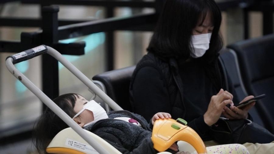 Mulher e criança com máscaras no aeroporto internacional de Tóquio; fábrica de máscaras está trabalhando extra para atender demanda - EPA