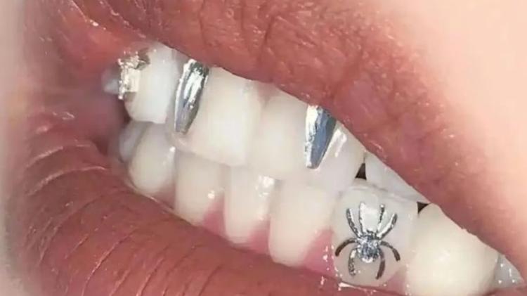 Entre os adereços, estão adesivos prateados que são colados nos dentes