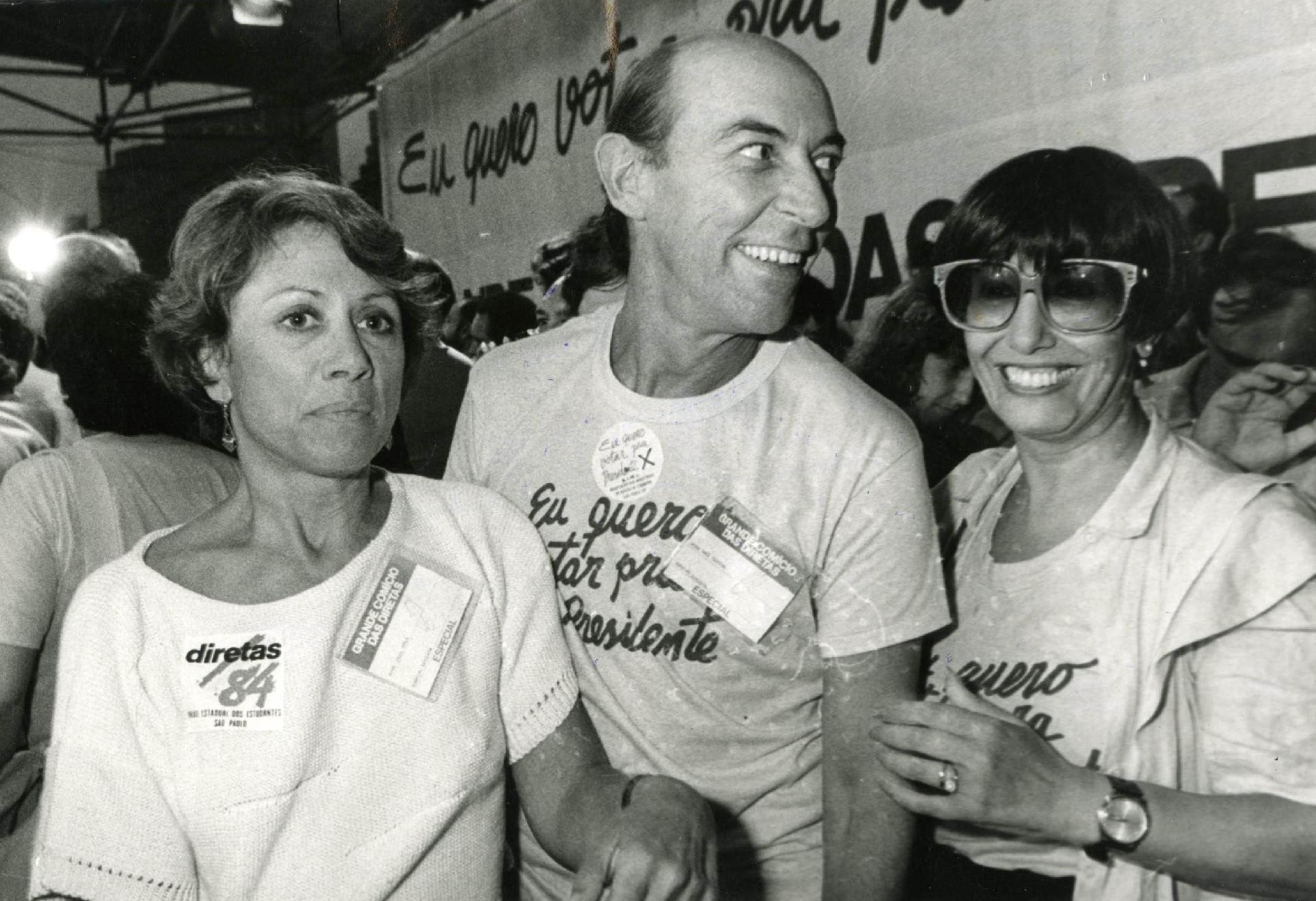A atriz Dina Staf, o ator Raul Cortez e a atriz e Ruth Escobar, na época deputada estadual, foram uns dos artistas a vestirem a camisa, literalmente, expressando o desejo de votar para presidente da República. A foto foi tirada no dia do grande comício das Diretas-Já, na praça da Sé, em 25 de janeiro de 1984 - Renato dos Anjos/Folhapress