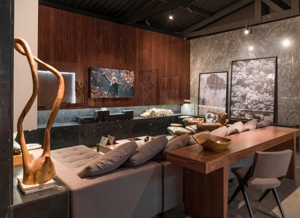 O arquiteto André Lenza se inspirou em um homem cosmopolita para desenhar o Studio 77. A madeira do espaço de 59 m², aplicada em móveis e no painel sobre a lareira, contrasta com o telhado com tesouras aparentes e com as paredes em tons de cinza. O sofá com chaise e as almofadas rosa antigo deixam a criação mais aconchegante - Jomar Bragança/Divulgação