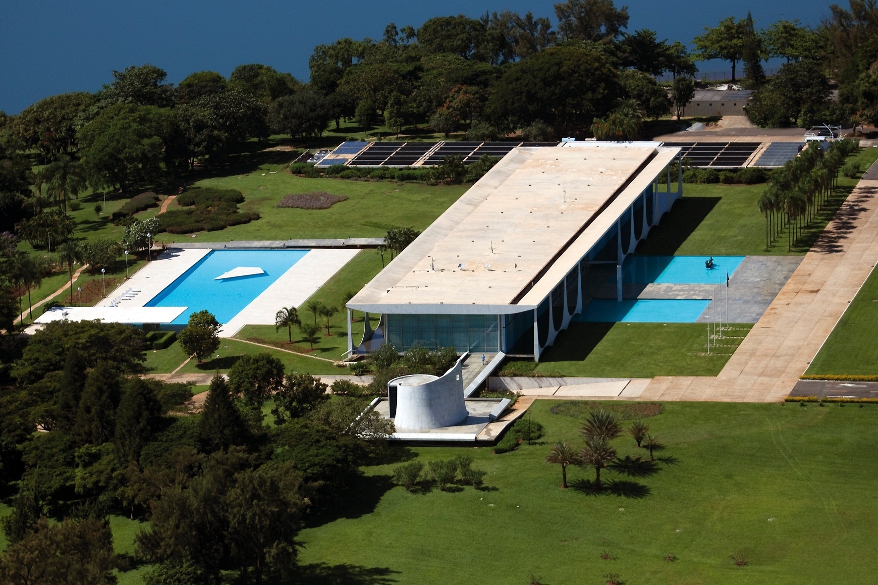 Vista aérea do conjunto do Palácio da Alvorada com o Lago Paranoá, ao fundo. O complexo é constituído de capela, edifício principal, piscina e anexo semi-enterrado, que abriga as dependências de serviços e uma sala de cinema. À direita, um detalhe: o corredor de palmeiras imperiais definido por Orcar Niemeyer, a pedido do presidente Juscelino Kubitschek - Leonardo Finotti/ UOL