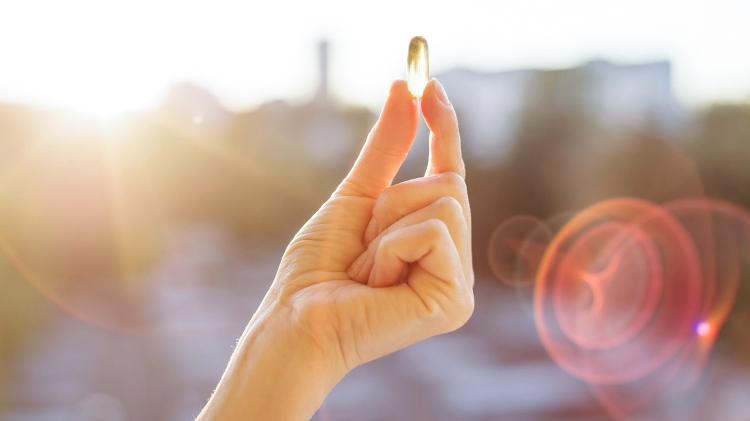 Mulher segurando pílula de vitamina D no sol - IStock - IStock