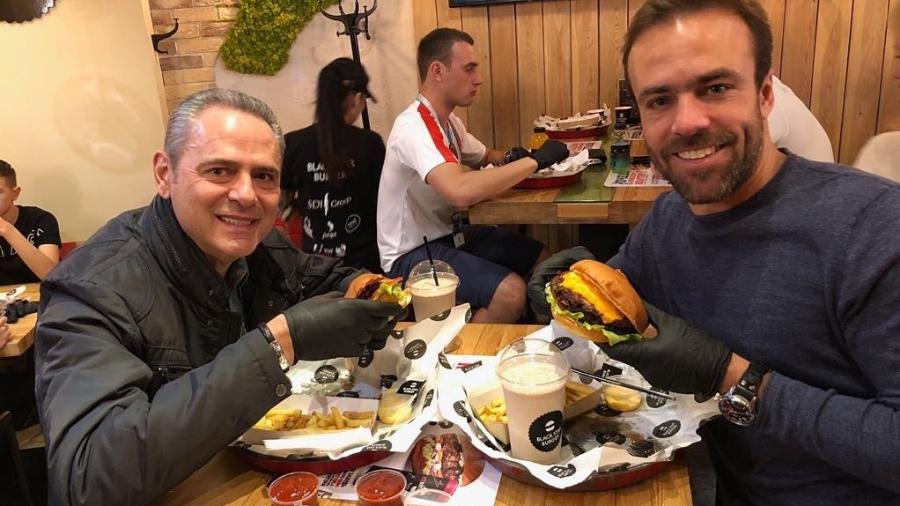 O narrador Luis Roberto e o comentarista Roger Flores comem hambúrguer usando luvas na Rússia - Reprodução/Instagram/luisrobertoreal