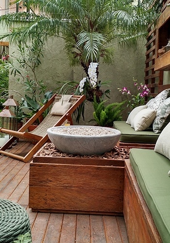 Em uma casa na zona sul de São Paulo, a paisagista Gigi Botelho dispôs sobre o deck de madeira de demolição uma área de descanso com cadeira de corda, mesa de apoio, bancos com almofadas e uma pira de pedra-sabão - Divulgação