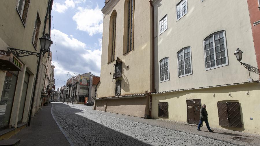 Homem com máscara facial atravessa a rua quase vazia em Vilnius, Lituânia, durante "lockdown" - Paulius Peleckis/Anadolu Agency via Getty Images