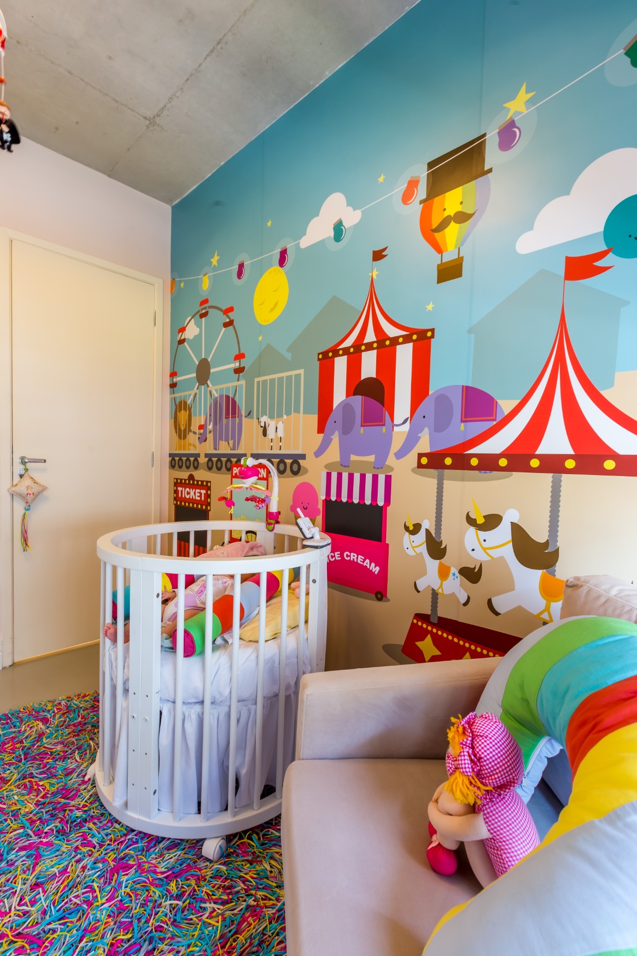 Neste quarto de uma menina, o tema circense apareceu no adesivo vinílico que revestiu a parede atrás do berço --ideia da equipe da By Arq & Design (www.byarq.com.br). O tapete com fitas de lycra coloridas, material antialérgico e antiderrapante, é trabalho de um artesão e foi escolhido para compor o projeto multicolorido. O berço é extensível para acompanhar o crescimento da bebê e aproveitar melhor o espaço do quarto - Melissa Binder/Divulgação