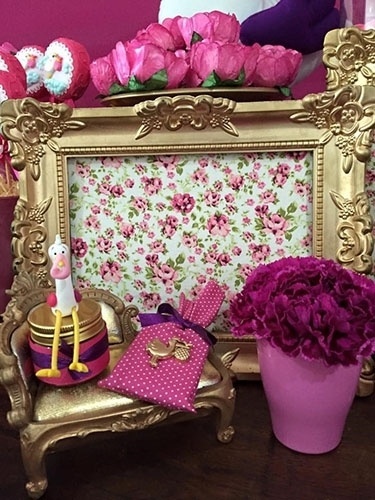 O cenário do chá de fraldas ganhou mais charme com essa composição que leva moldura provençal com fundo em tecido floral, da Le Parti Locações (instagram.com/lepartiloc) e chaise dourada em miniatura. Ao lado, vasinho de louça com arranjo de cravos na cor pink - Divulgação