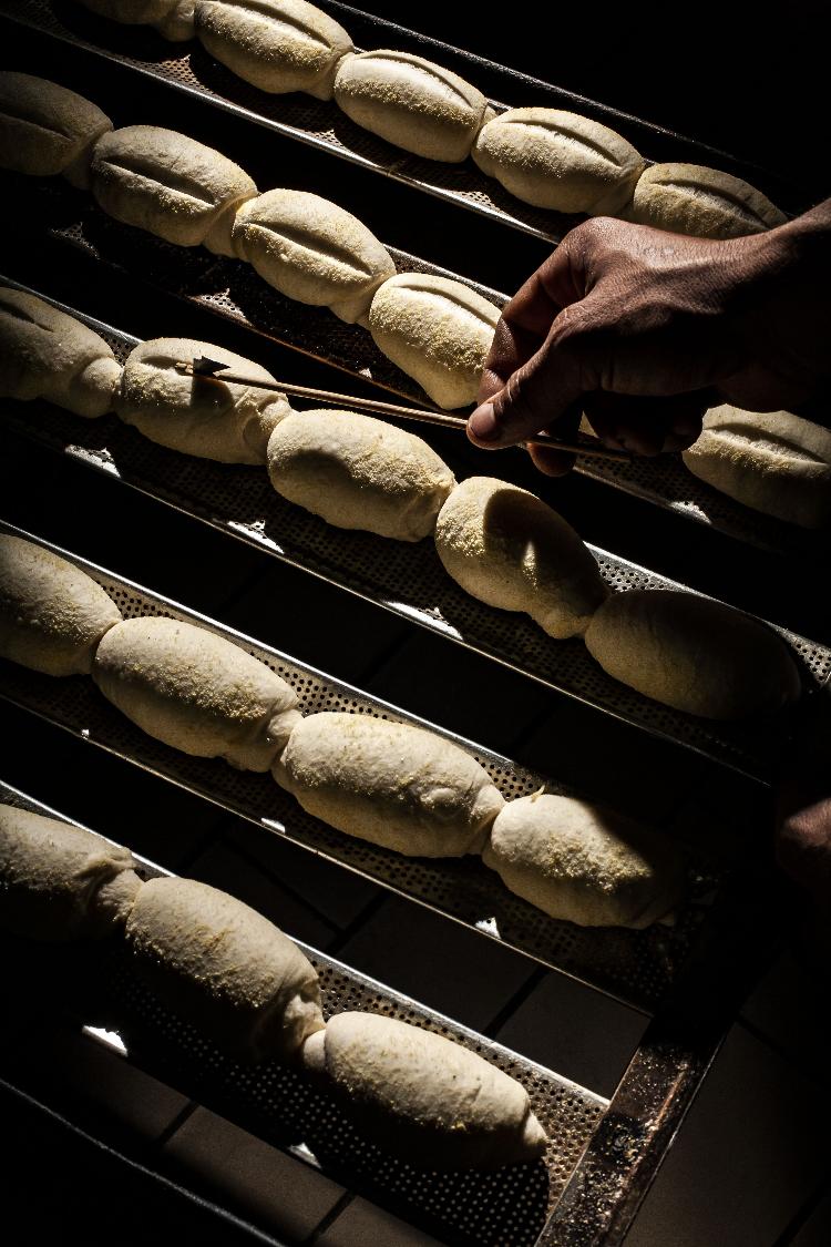 A massa do pãozinho sendo preparada para entrar no forno à lenha que nunca é apagado