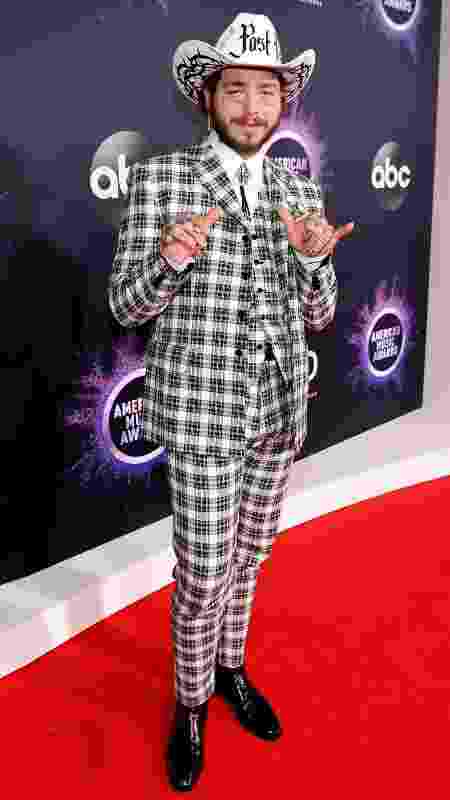 O rapper Post Malone com terno de alfaiataria xadrez, chapéu e bota envernizada  - Getty Images